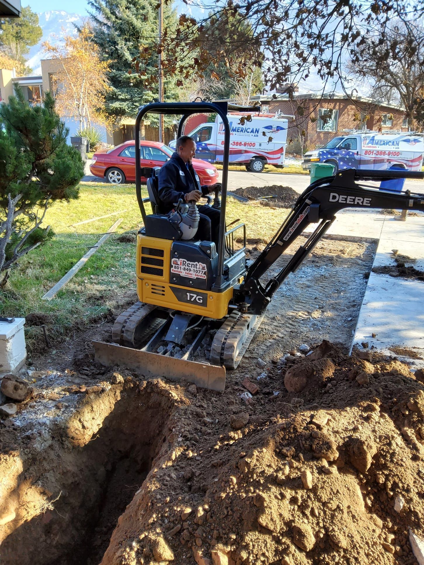 Person operating a mini excavator in a yard, digging a trench.