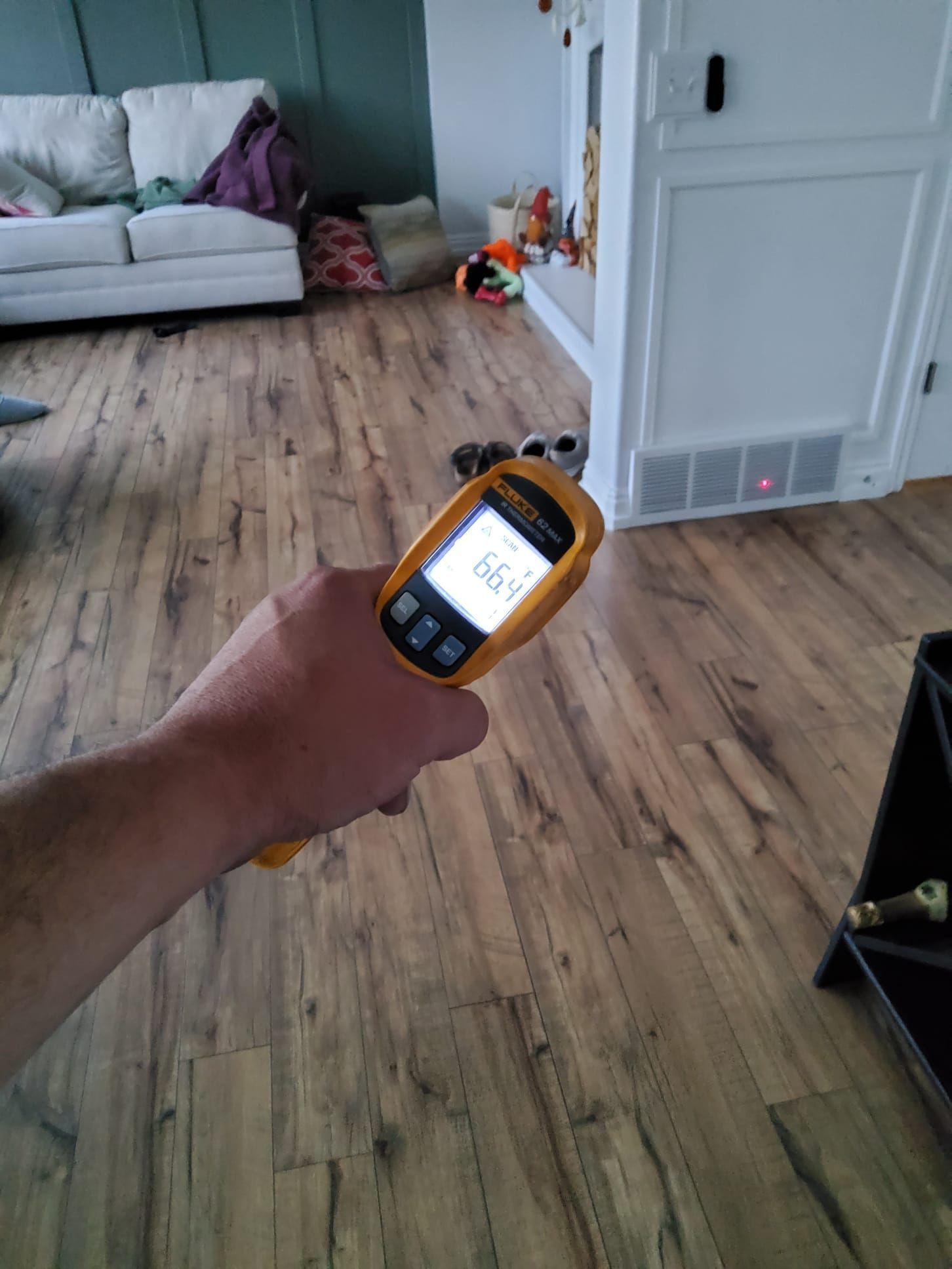 Hand holding a yellow temperature gun, reading 66.4 degrees, pointed at a floor.