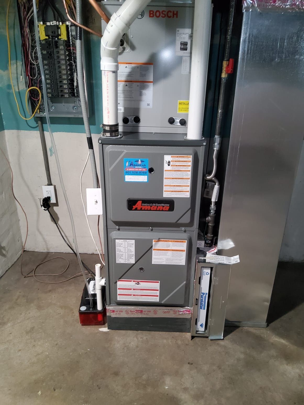 Furnace unit in a basement, with electrical panel on the wall to the left.