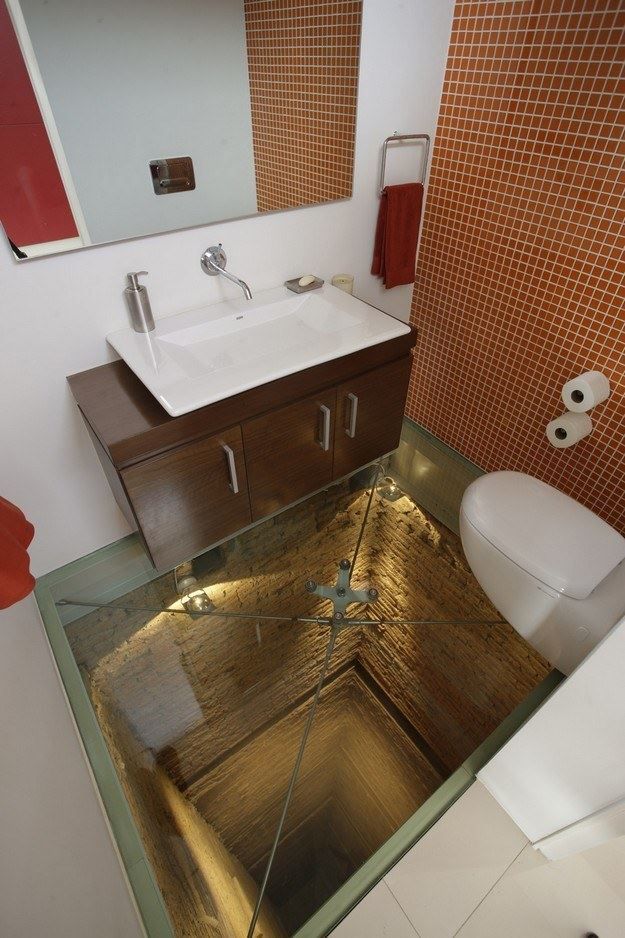 Bathroom with a sink, toilet, and a glass-floored shower with decorative brick-like wall tiles.