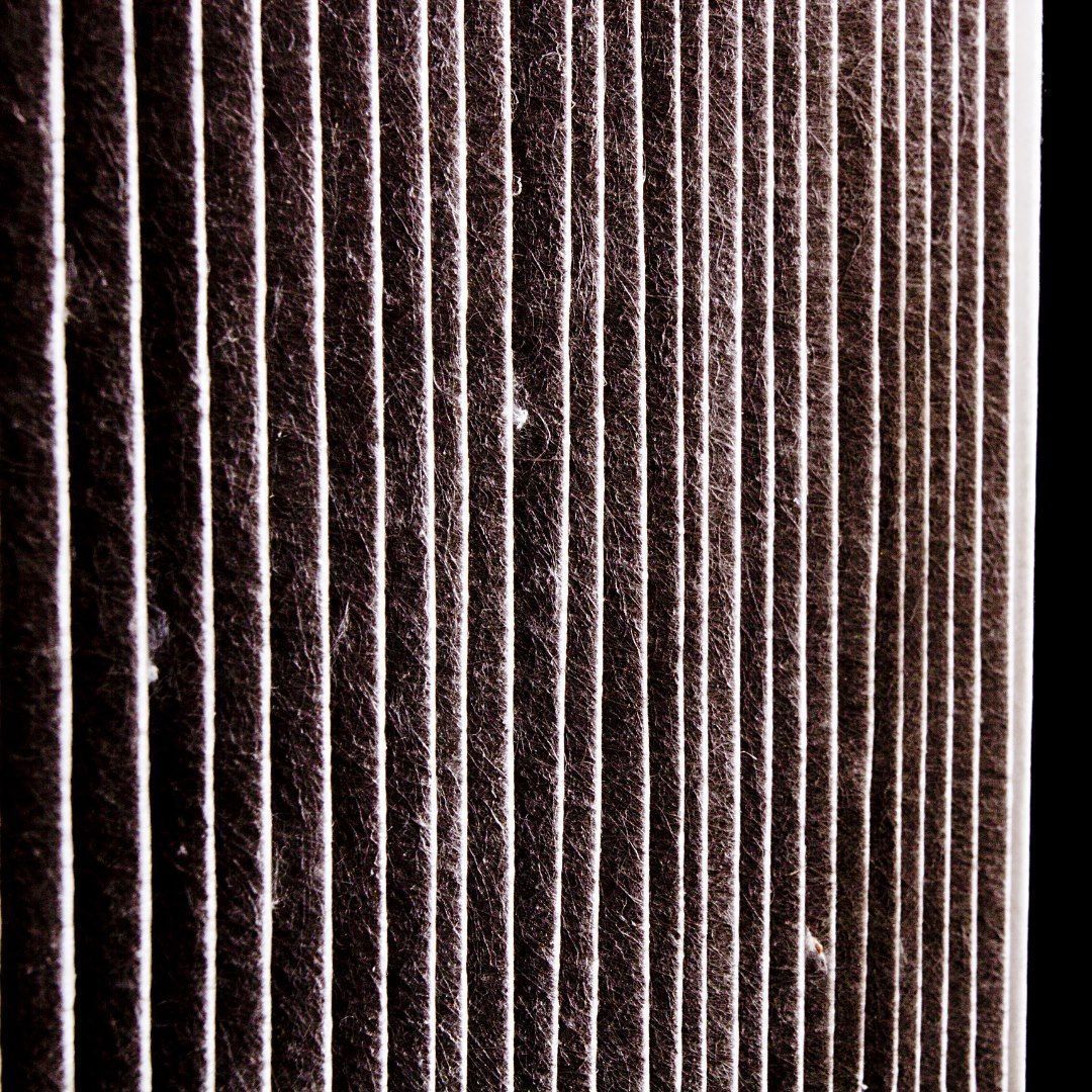 Close-up of a rectangular air filter with vertical pleated lines, covered in dust and debris.