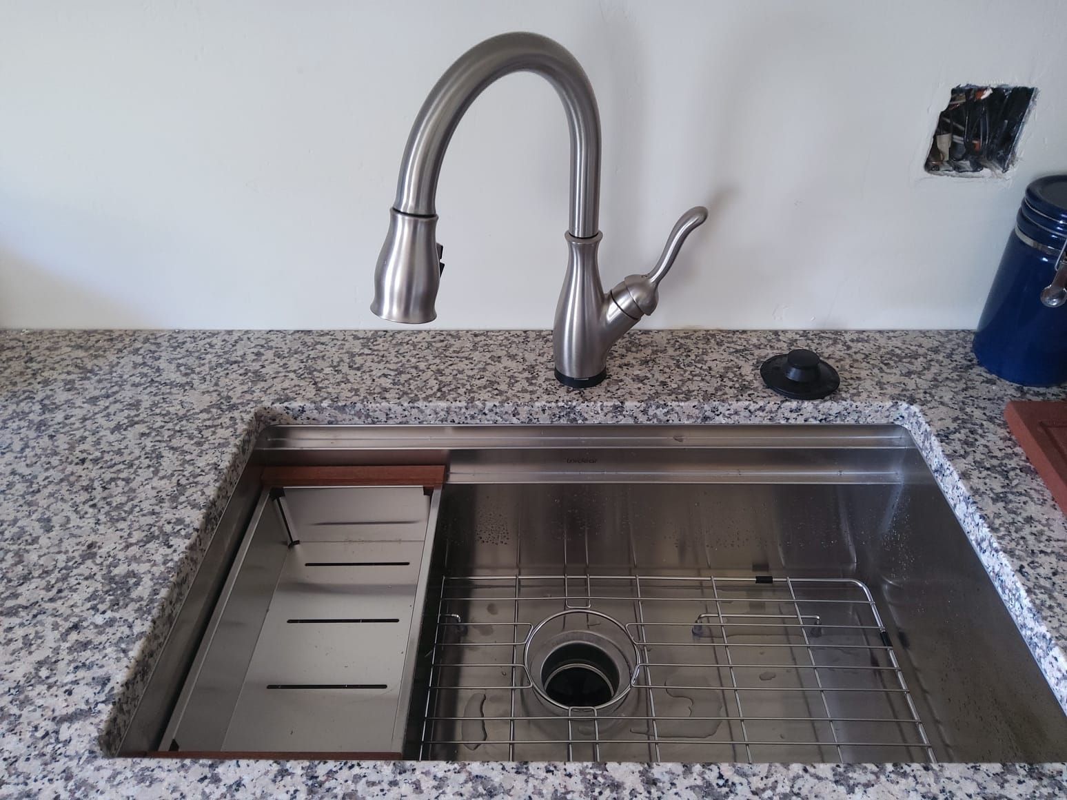 Stainless steel kitchen sink with faucet, granite countertop, and accessories.