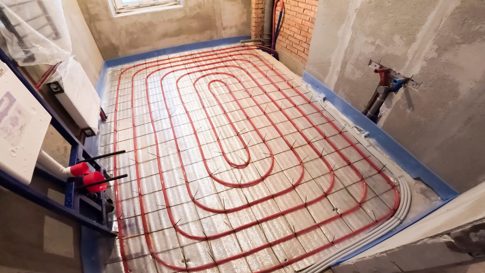 Red pipes snaked across a floor, installed for radiant floor heating, in a room under construction.