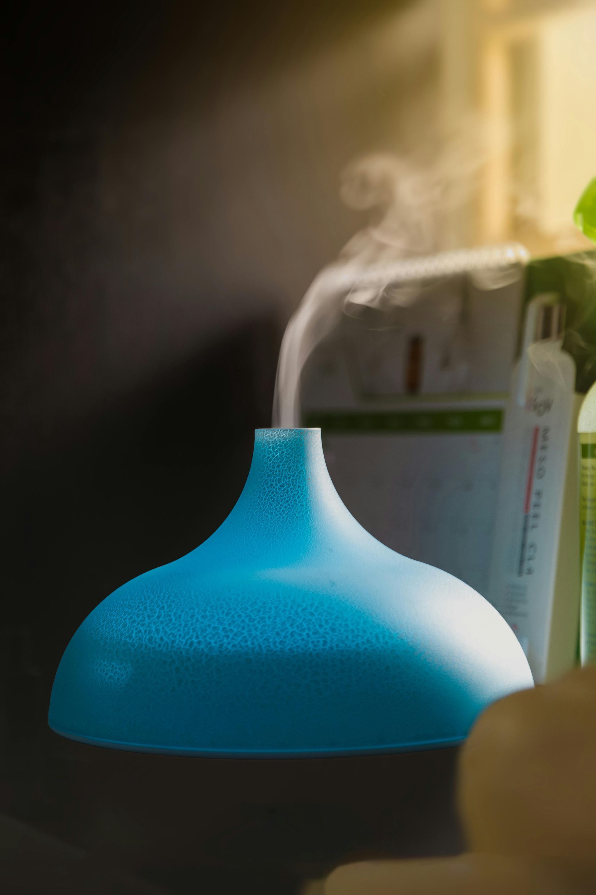 Blue essential oil diffuser releasing vapor, indoors, with a thermometer in the background.