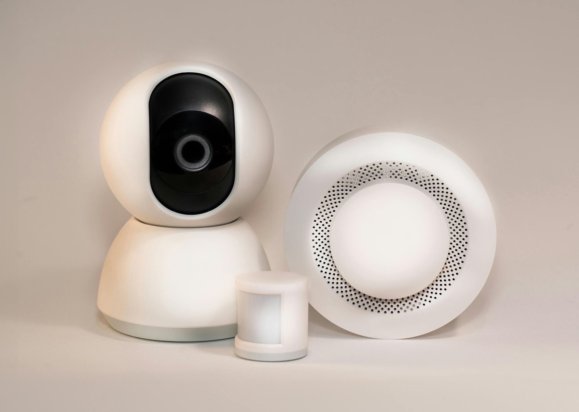 White security camera, motion sensor, and smoke detector on a gray surface.