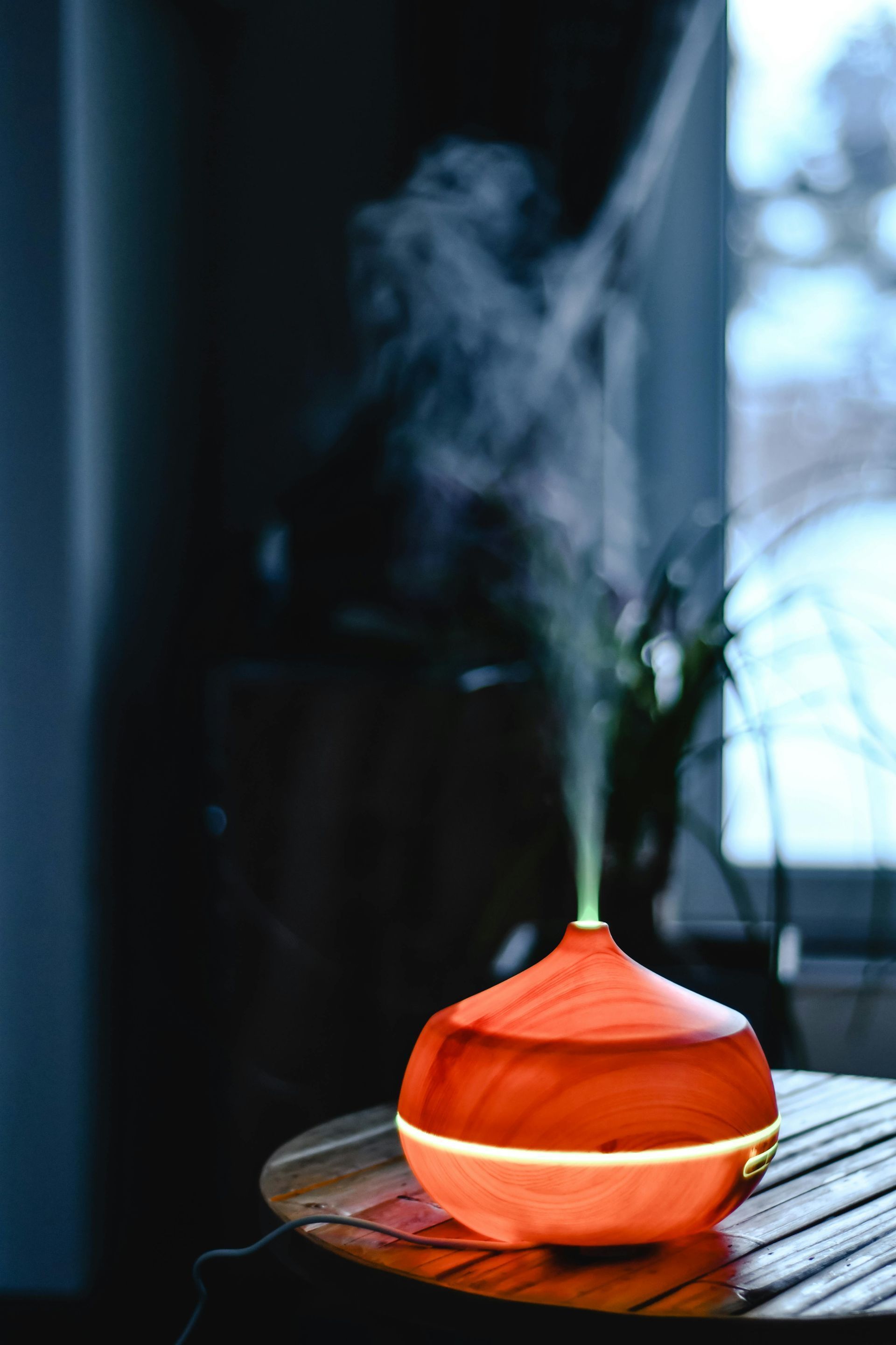 Orange essential oil diffuser emitting mist, sitting on a wooden table indoors.