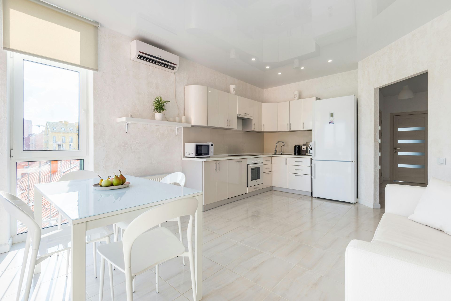 Bright white kitchen with dining area, cabinets, refrigerator, and small sofa.
