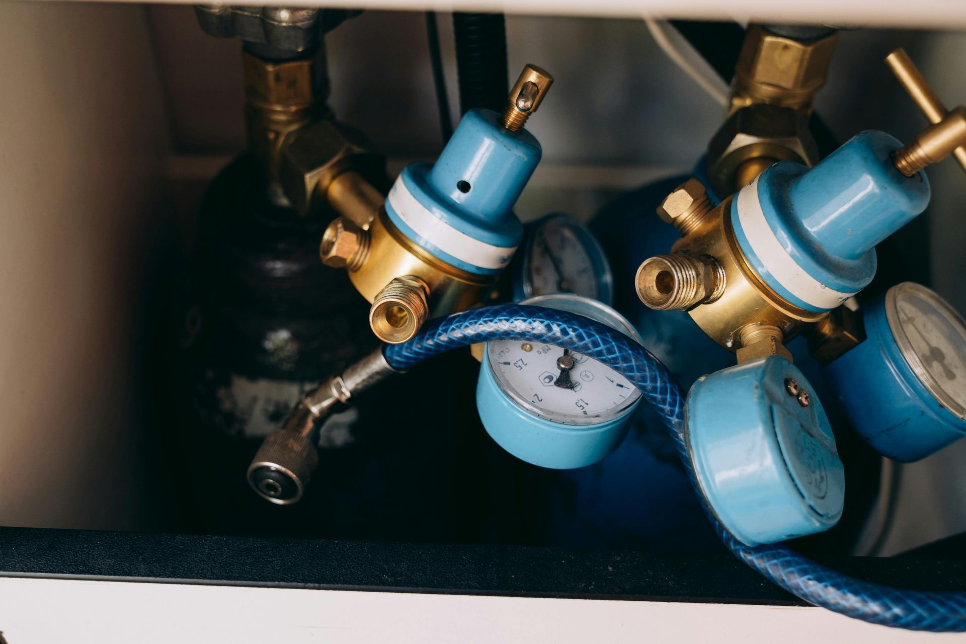 Close-up of oxygen tanks with blue regulators, gauges, and hoses in an enclosed space.