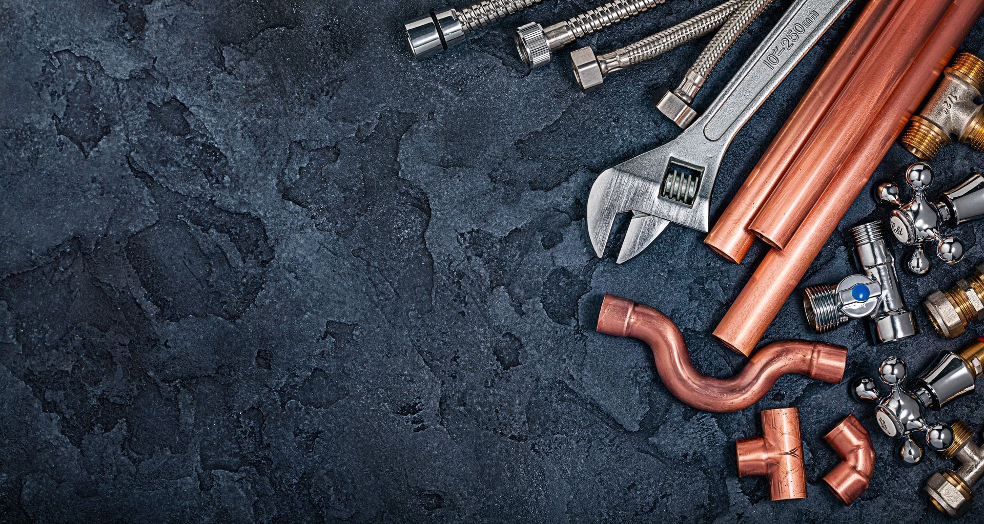 Plumbing tools and copper pipes on a dark textured background.
