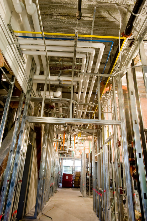 A hallway in a building under construction with pipes hanging from the ceiling.