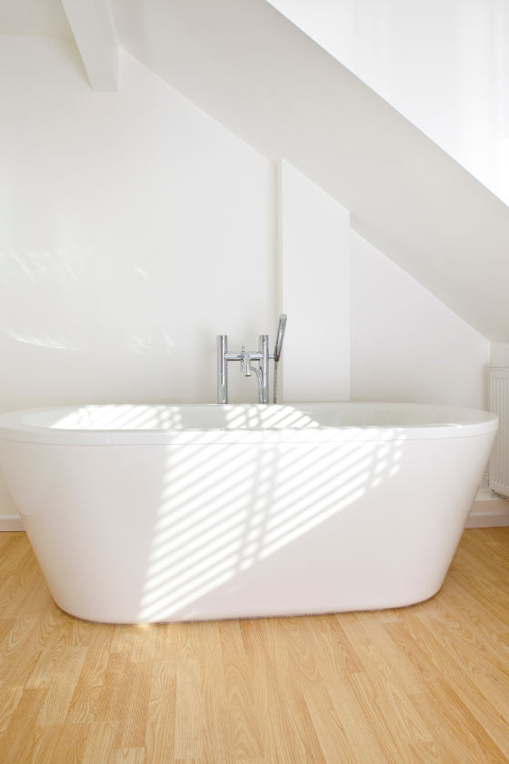 A white bathtub is sitting on a wooden floor in a bathroom.