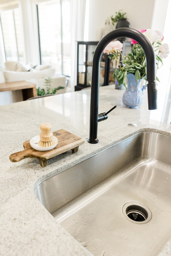 A kitchen sink with a black faucet and a cutting board on top of it.