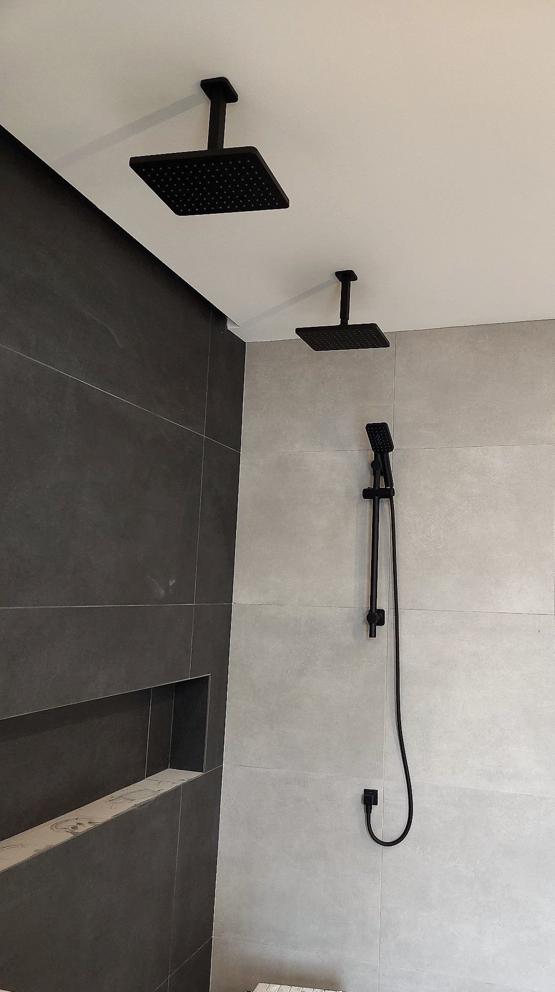 A bathroom with two square shower heads hanging from the ceiling.