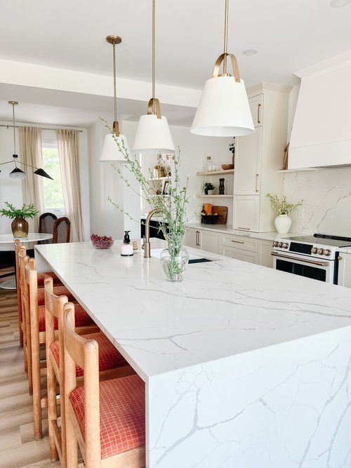 A kitchen with a long white counter top and wooden chairs.