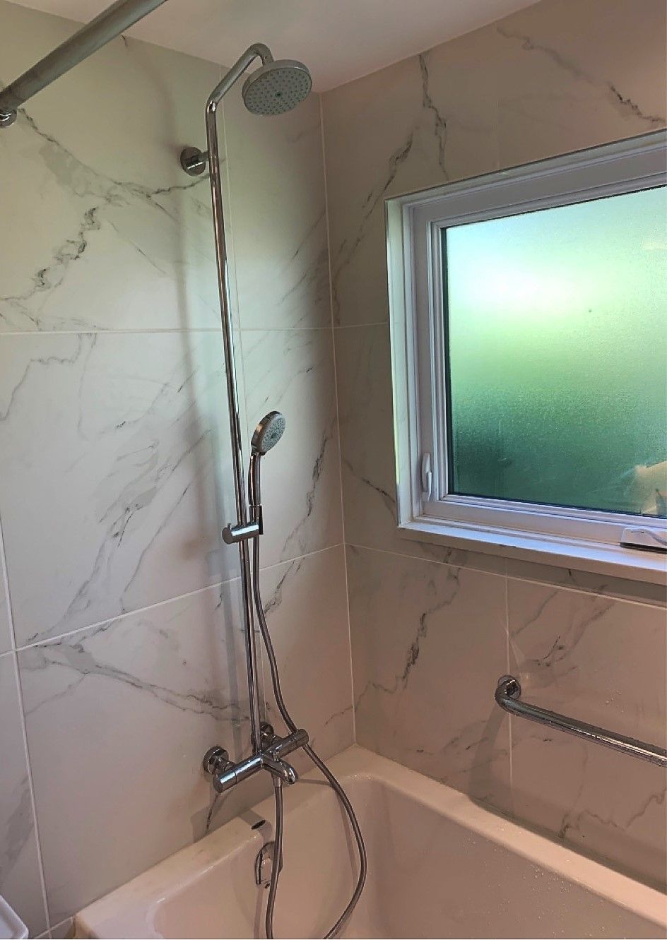 A bathroom with a bathtub , shower , and window.