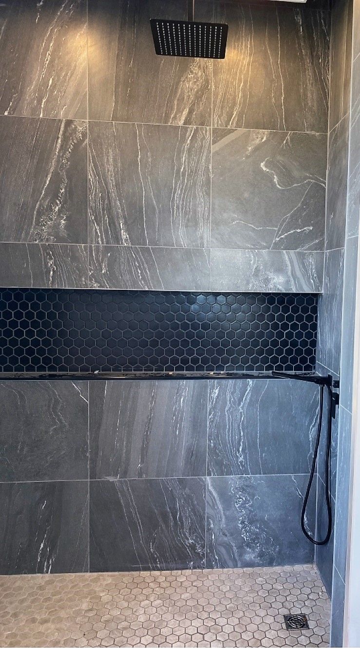 A shower with black tiles and a shower head.