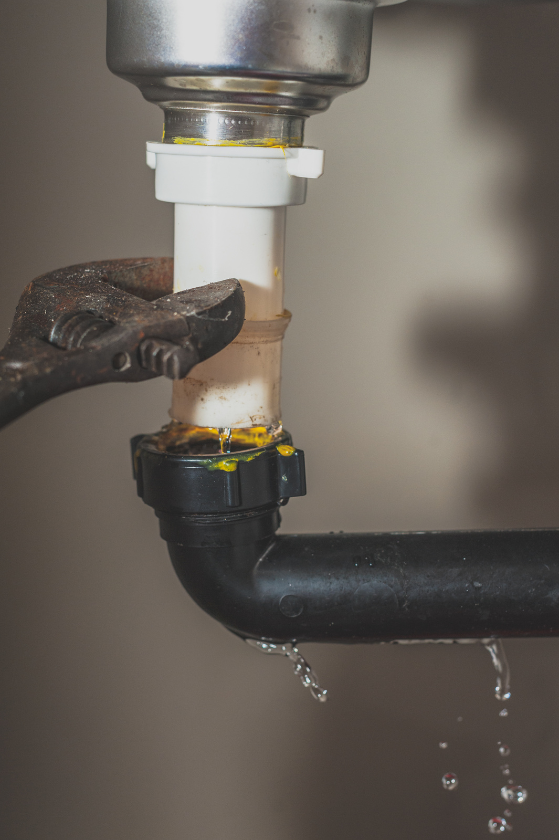 A person is fixing a leaking sink pipe with a wrench.