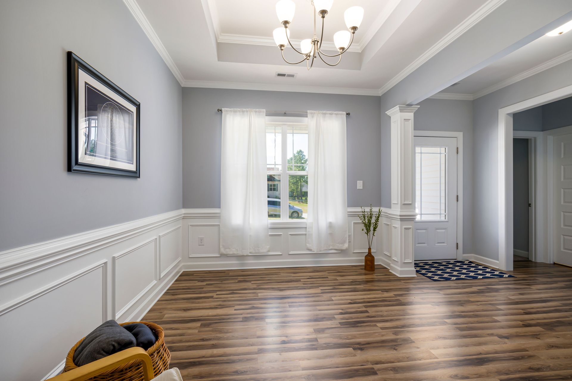Empty gray living room with wood floors, white trim, chandelier, and a doorway to the hall