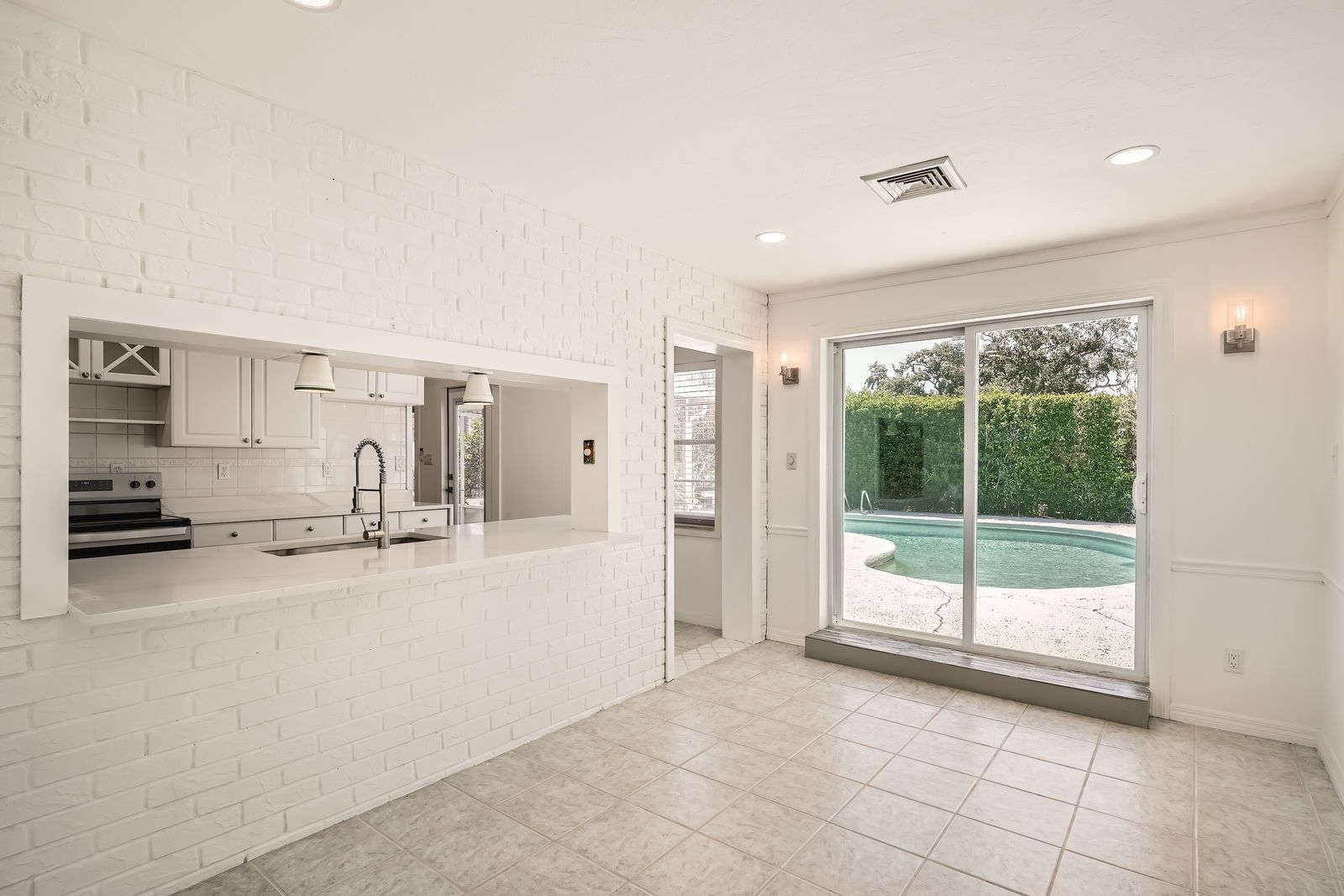 A living room with a kitchen and a sliding glass door leading to a pool.