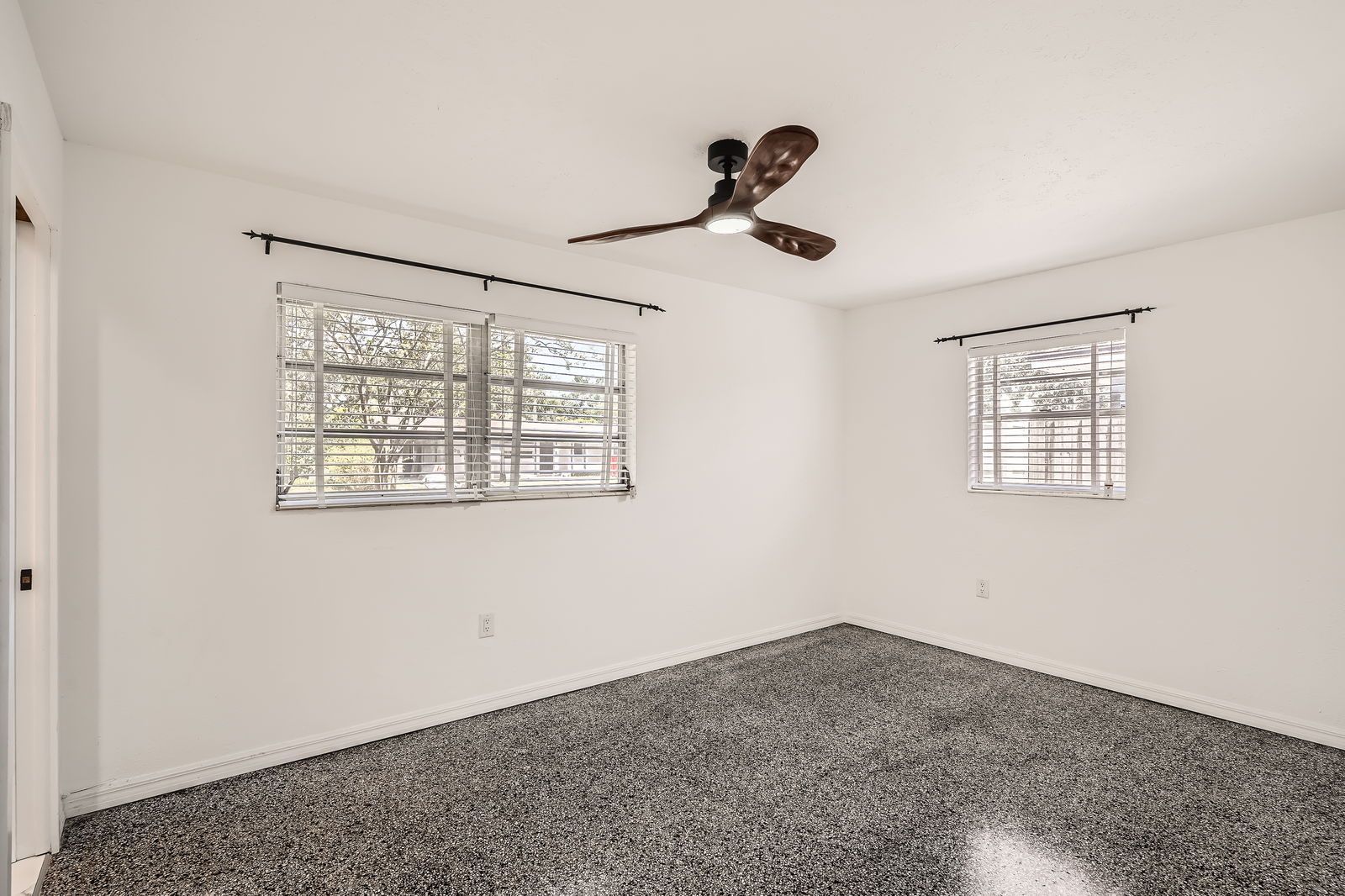 An empty room with a ceiling fan and two windows.