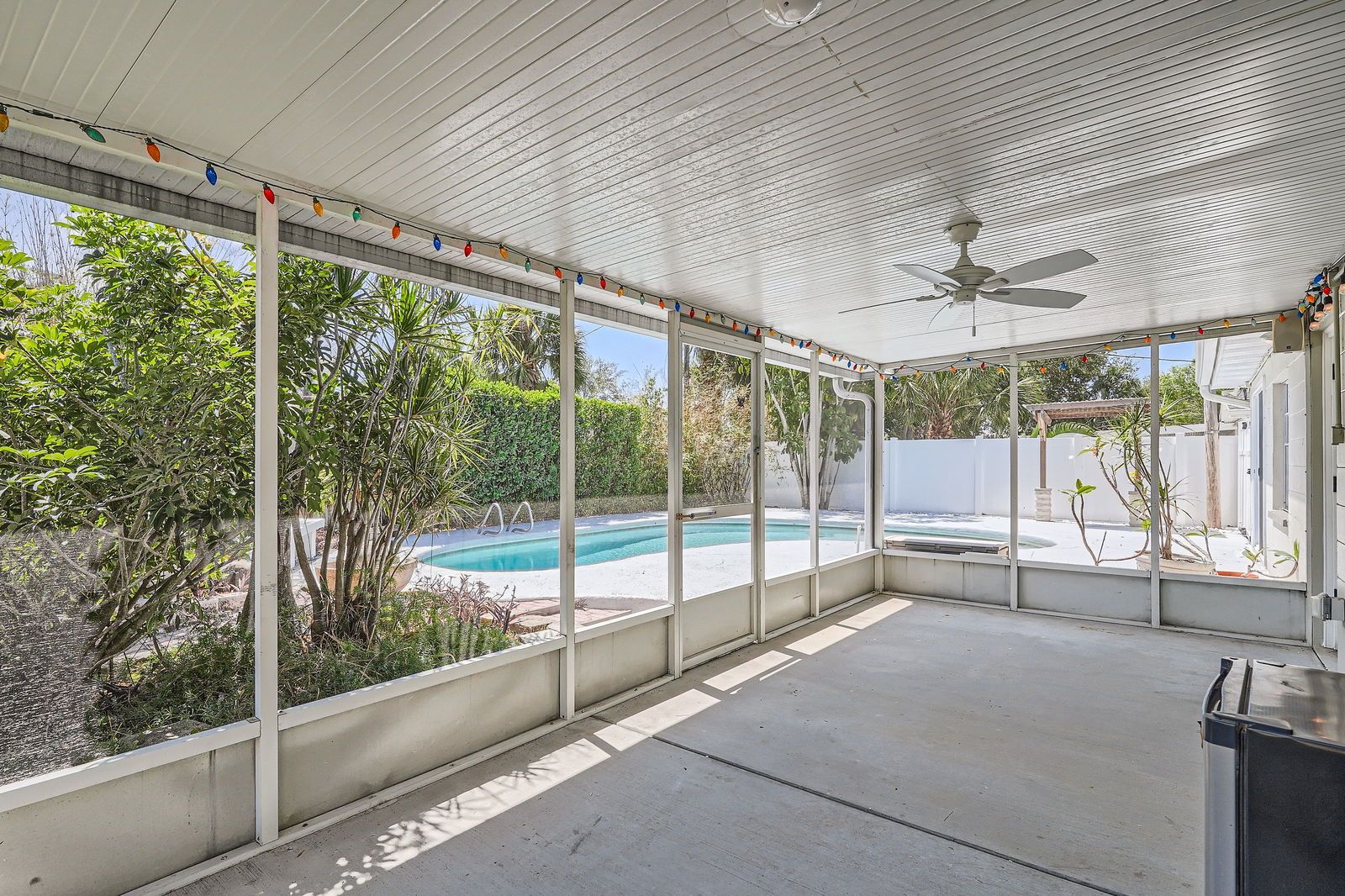 A screened in porch with a ceiling fan and a swimming pool in the background.