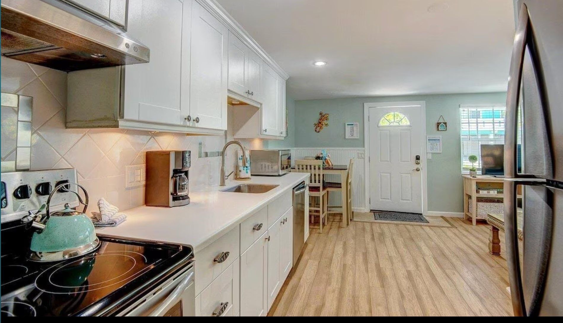 A kitchen with white cabinets , a stove , a refrigerator and a sink.
