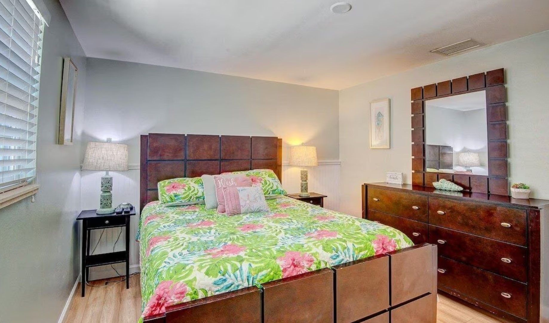 A bedroom with a king size bed , dresser , nightstand and mirror.