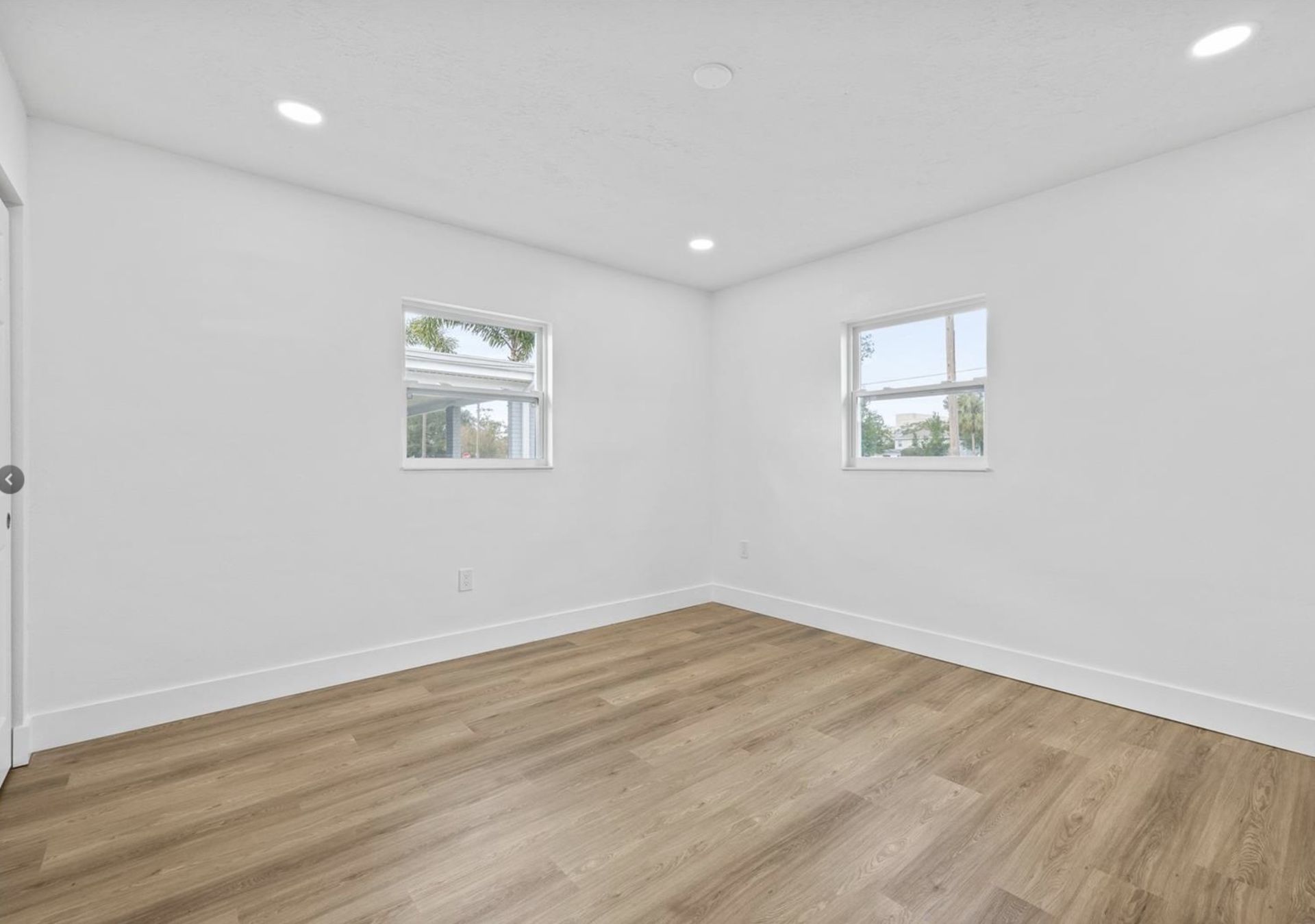 An empty bedroom with hardwood floors and two windows.