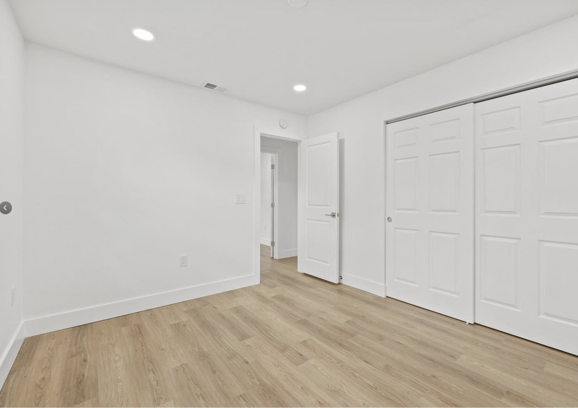An empty bedroom with hardwood floors and white walls.