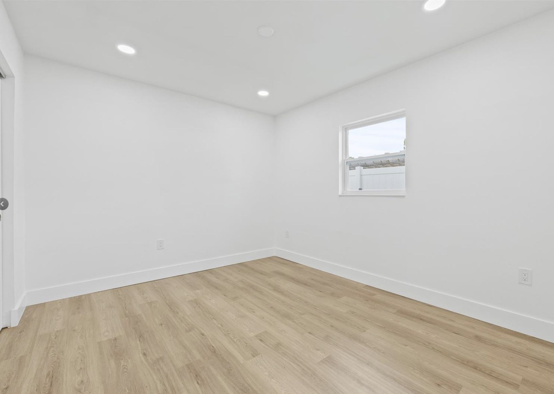 An empty room with hardwood floors , white walls and a window.
