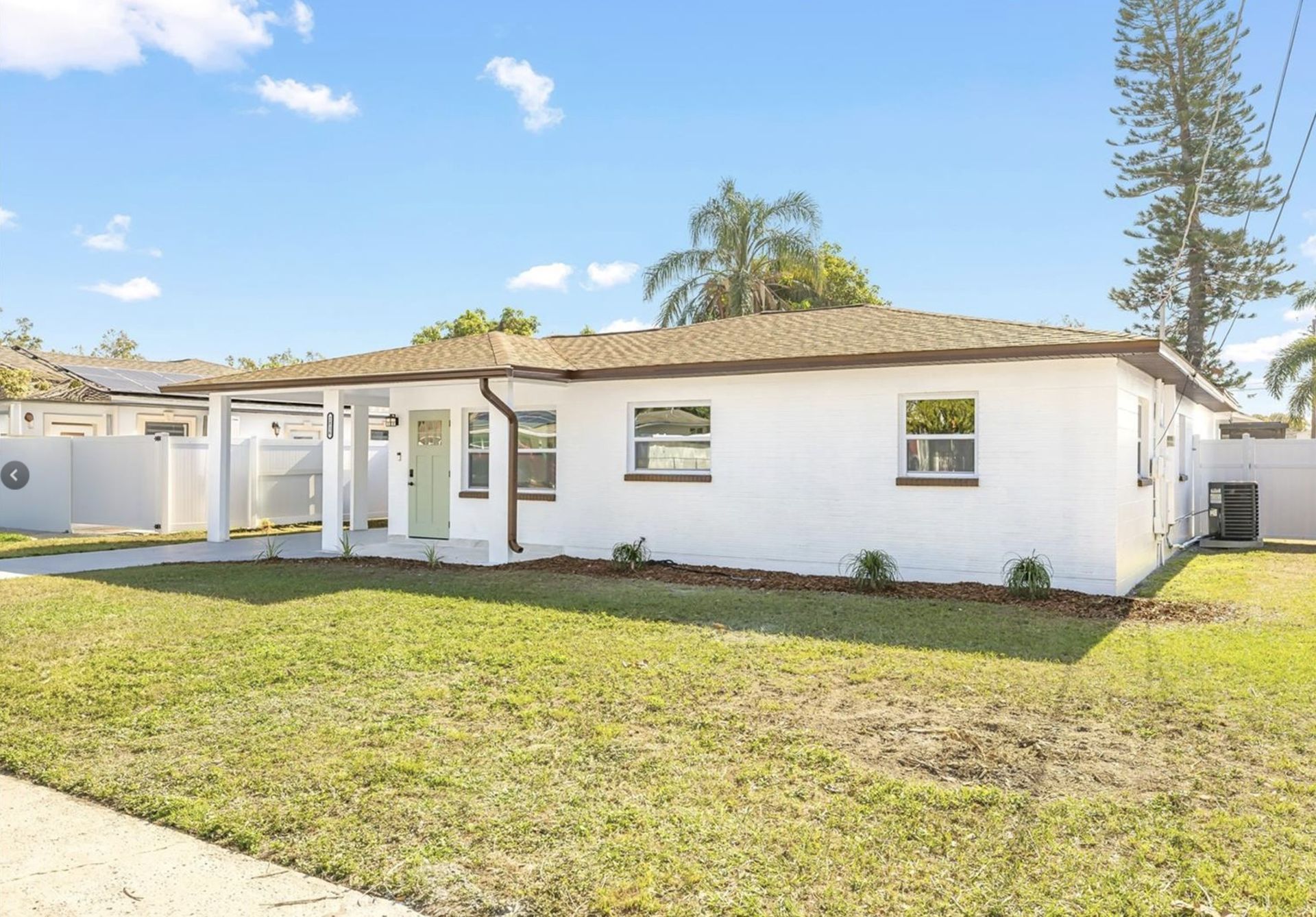 A white house with a brown roof is sitting on top of a lush green lawn.