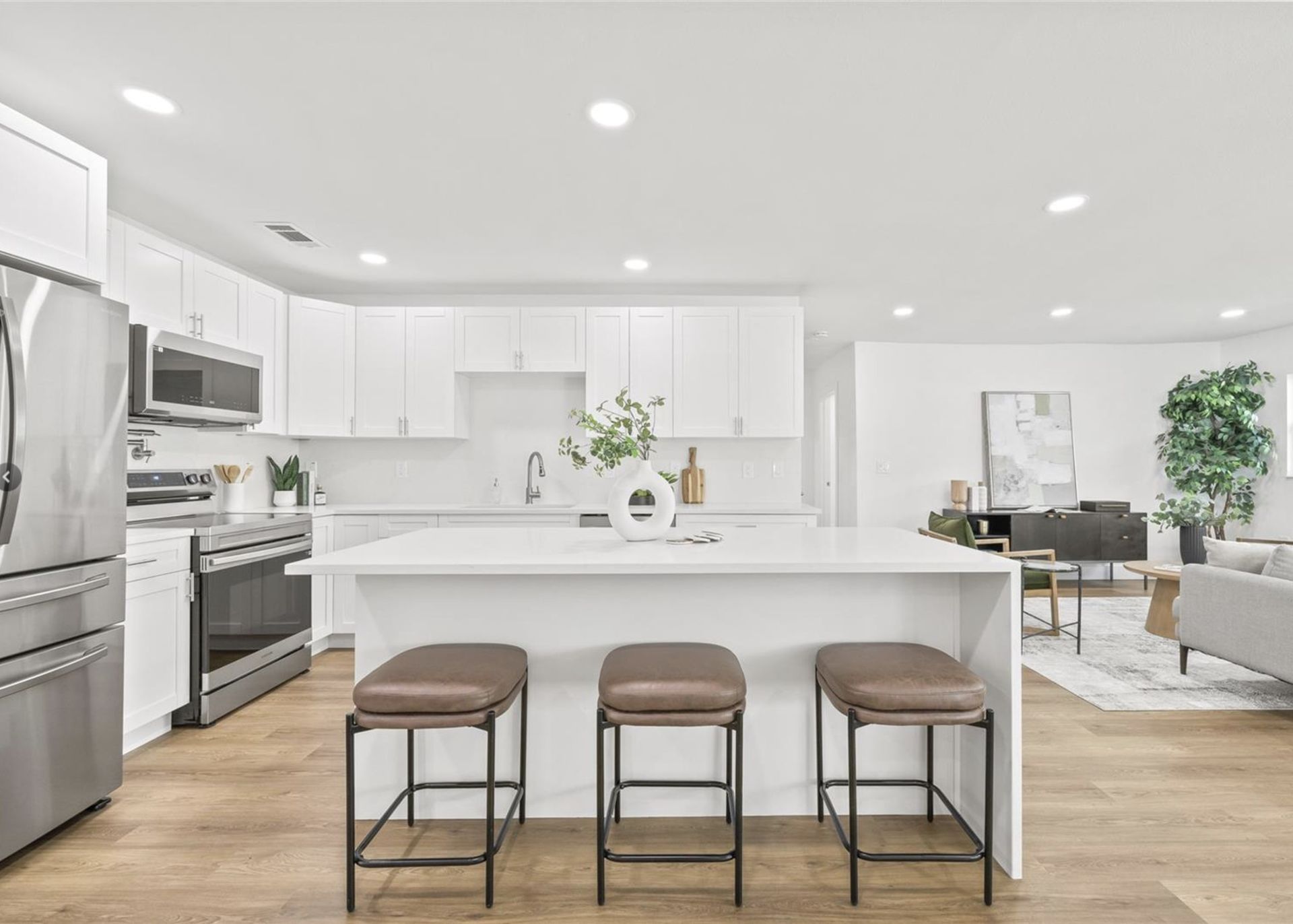 A kitchen with white cabinets , stainless steel appliances , and a large island with three stools.