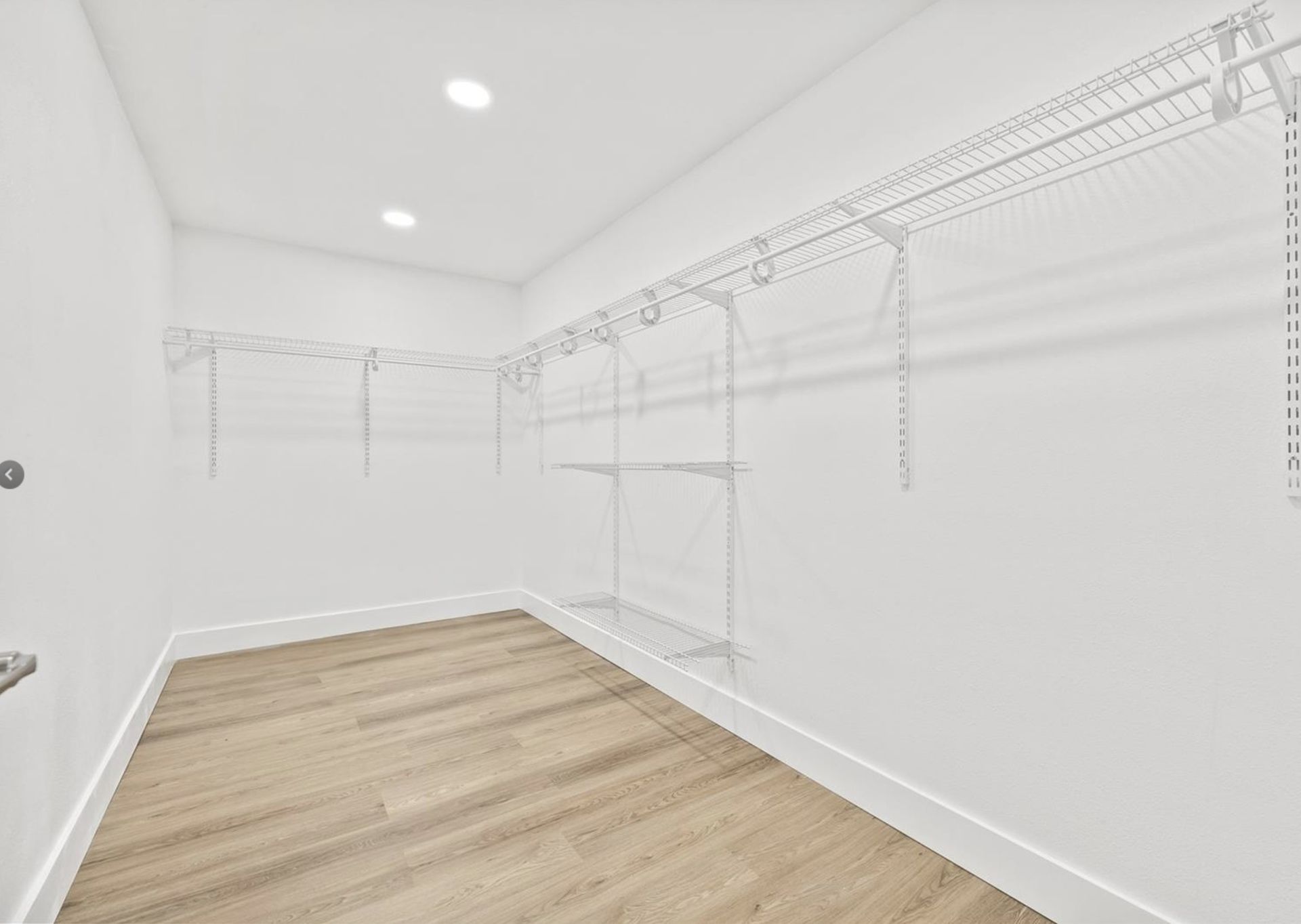 An empty walk in closet with wooden floors and white walls.