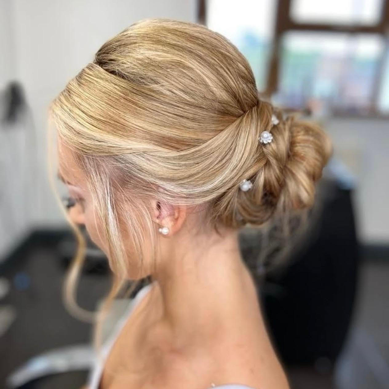 Blonde updo hairstyle with soft side-swept bangs and decorative hairpins in a salon setting