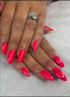 Hands with bright pink acrylic nails and a silver ring resting on a light fabric background.
