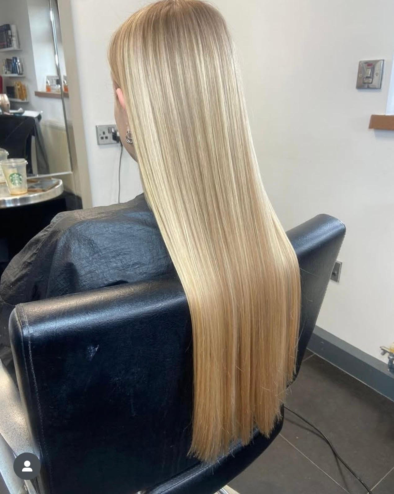 Long straight blonde hair cascading over the back of a black salon chair in a salon setting
