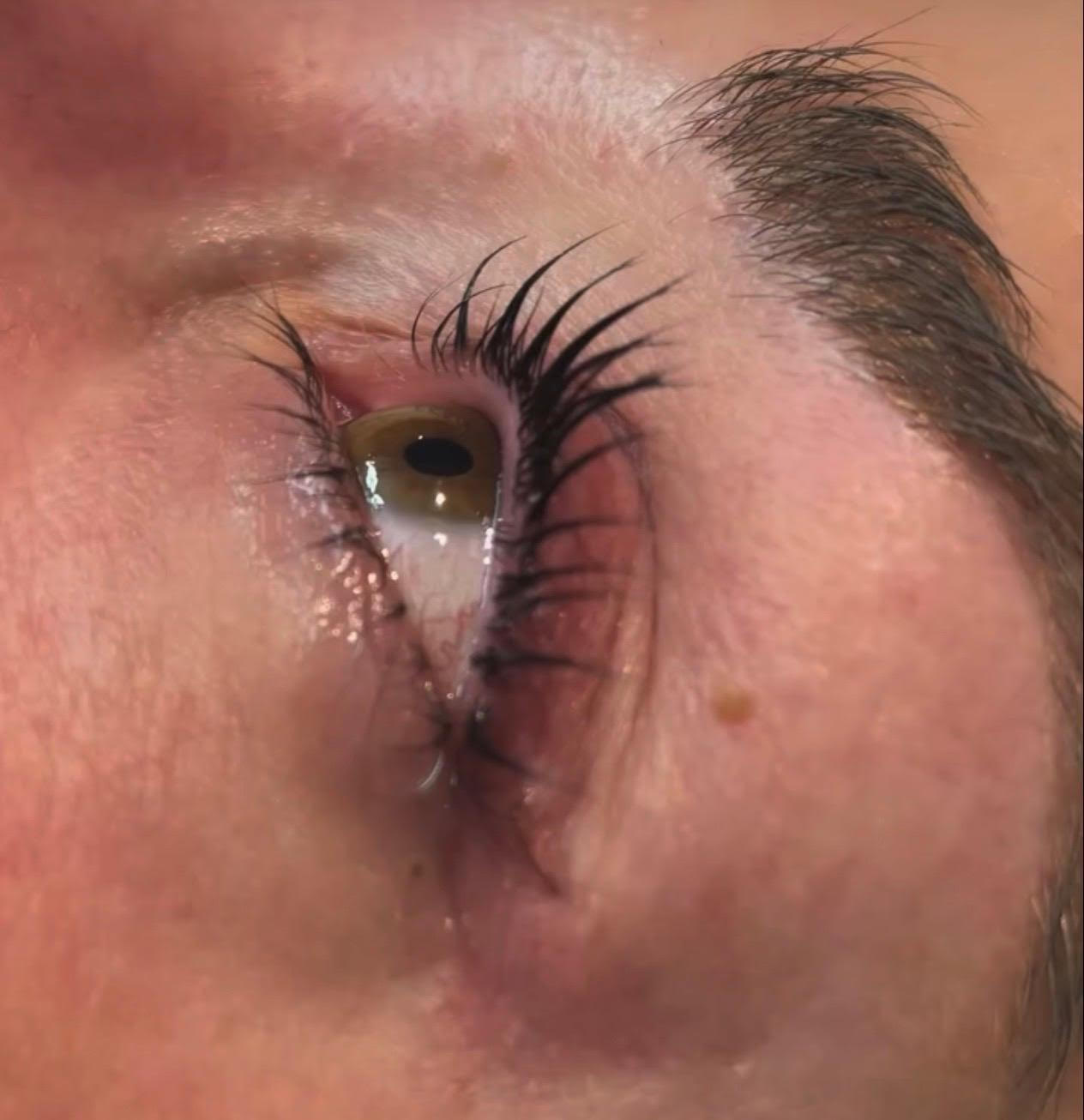 Close-up of a human eye with long eyelashes, looking upward in warm lighting