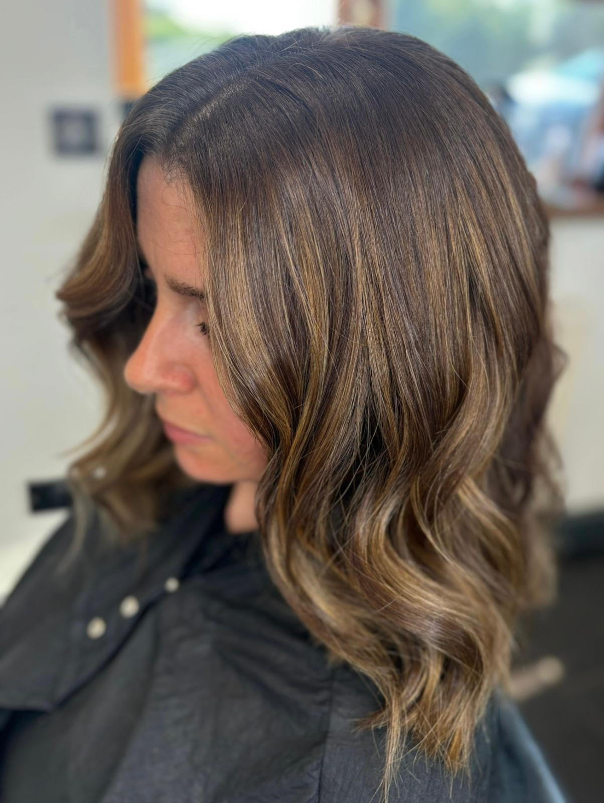 Side profile of a woman with shoulder-length brown wavy hair in a salon chair