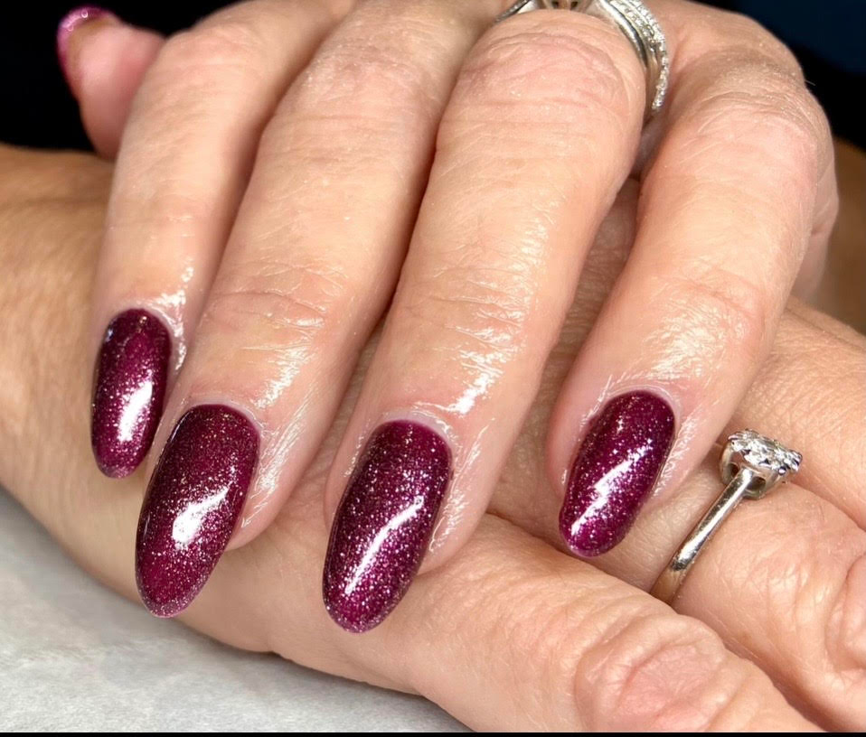 Close-up of hands with long burgundy glitter nails and silver rings.