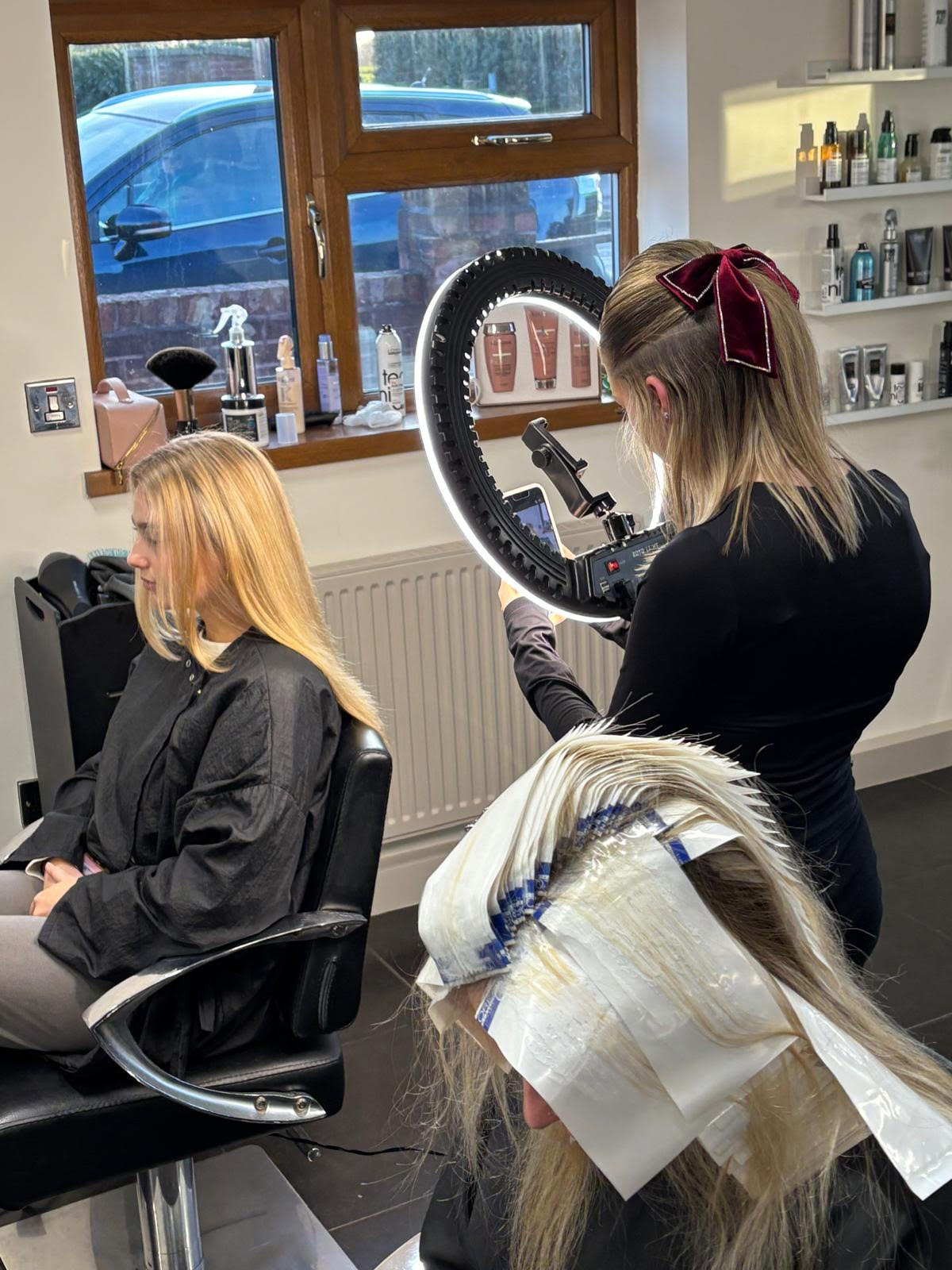 Hair salon with a stylist blow-drying a seated client's hair in front of a mirror.