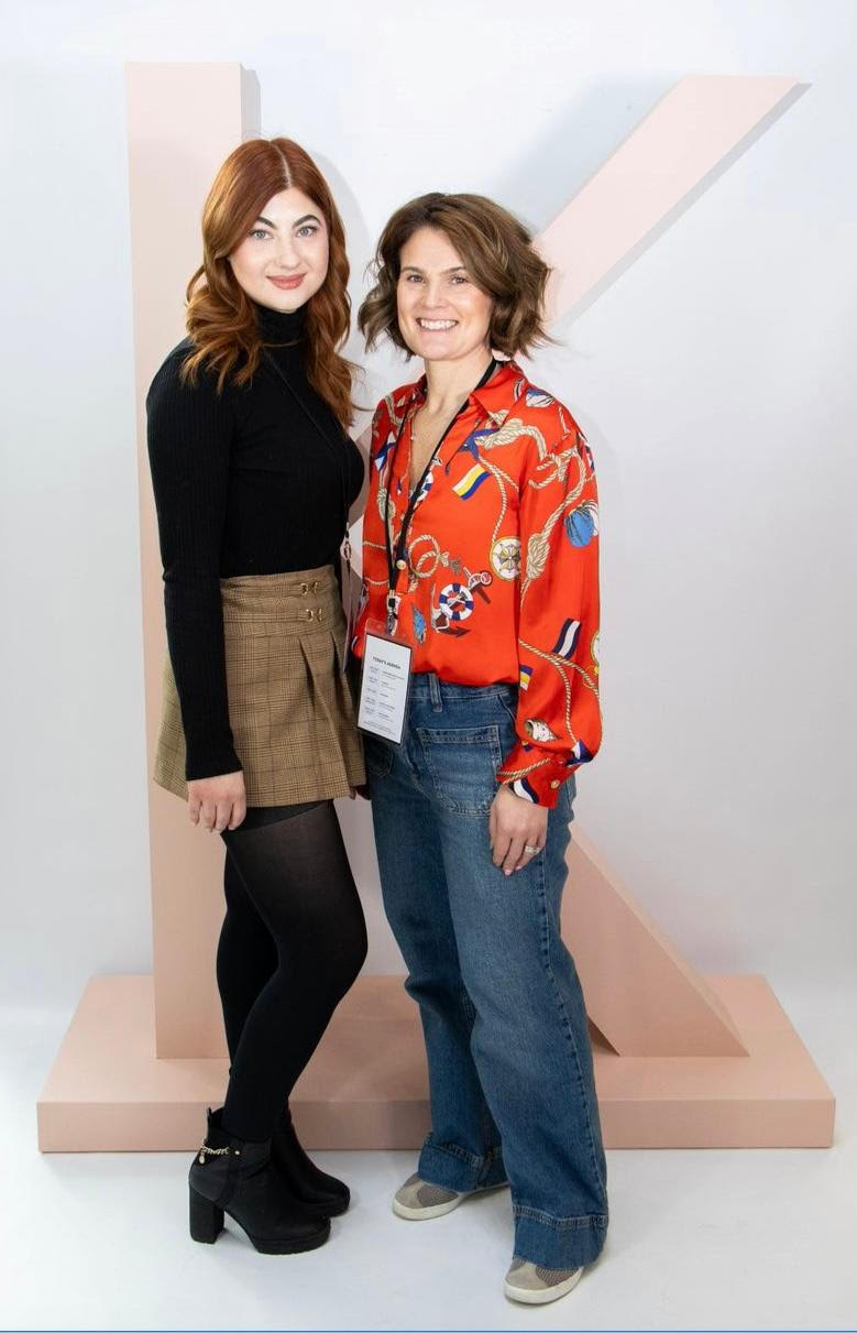 Two women standing together in front of a large pastel letter K backdrop
