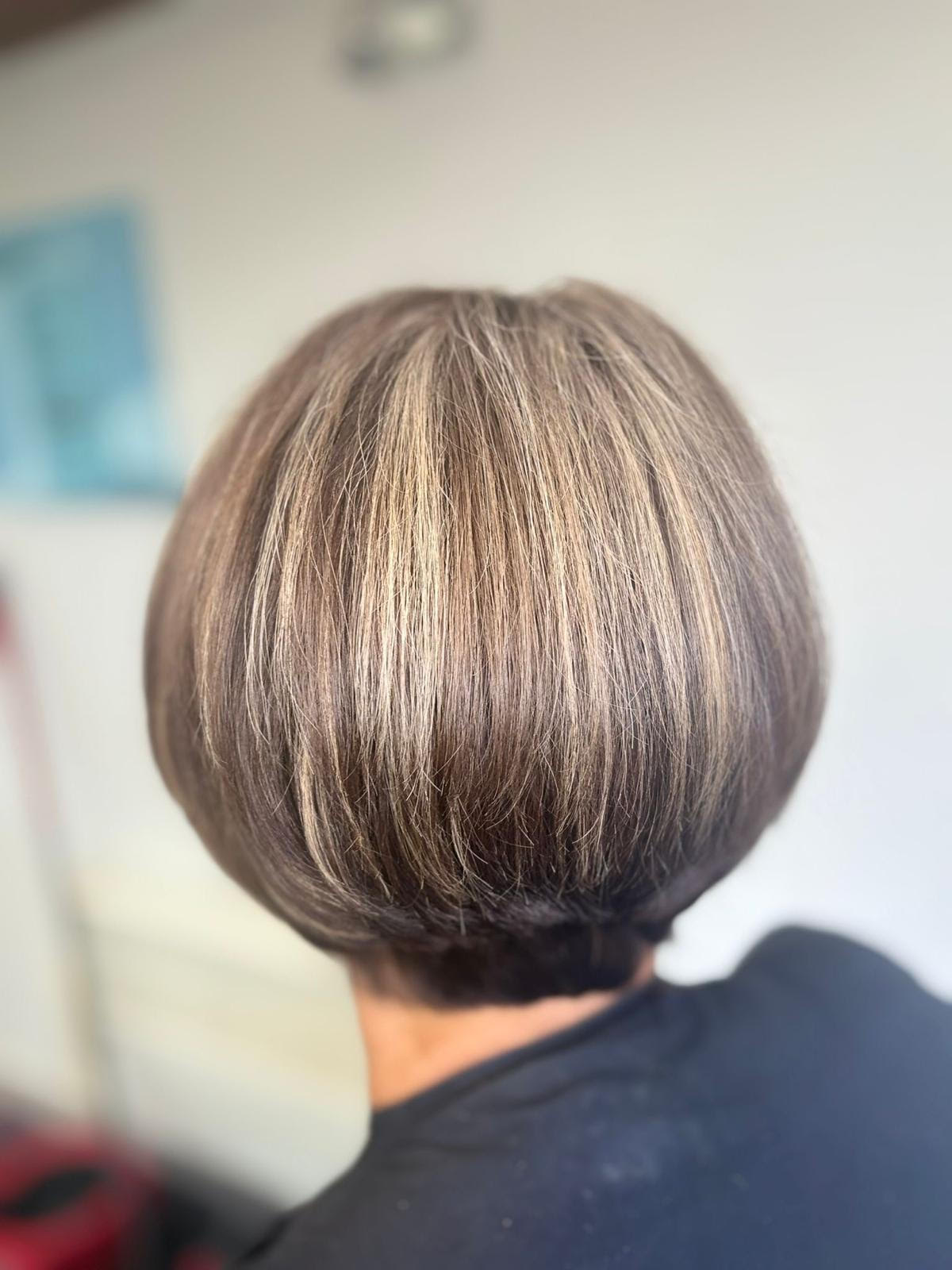 Short layered bob haircut with blonde highlights and dark lowlights, shown from the back in a salon setting