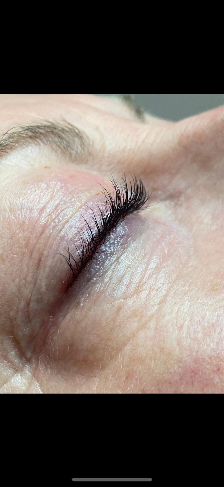 Close-up of a closed eye with natural lashes and light skin, softly lit.
