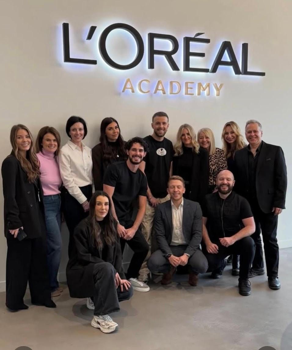 Group posing in front of a L’Oréal Academy wall sign, indoors.