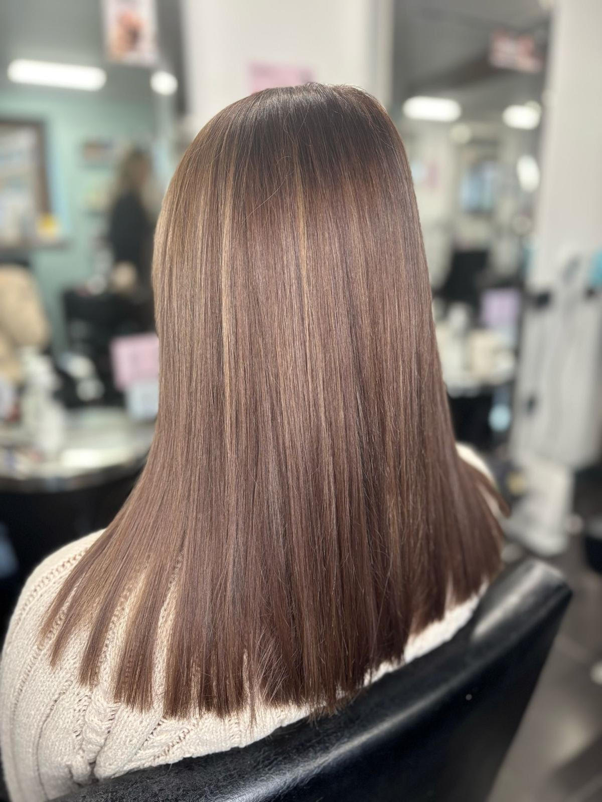 Straight brown hair with lighter highlights, viewed from behind in a salon chair