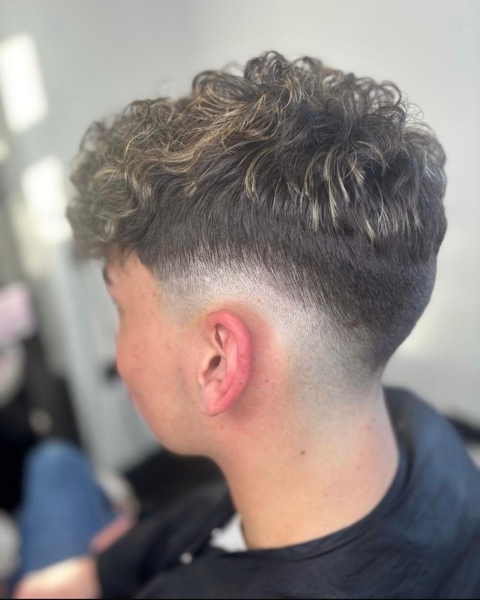 Close-up of a fresh fade haircut with curly top and tapered sides in a barbershop.