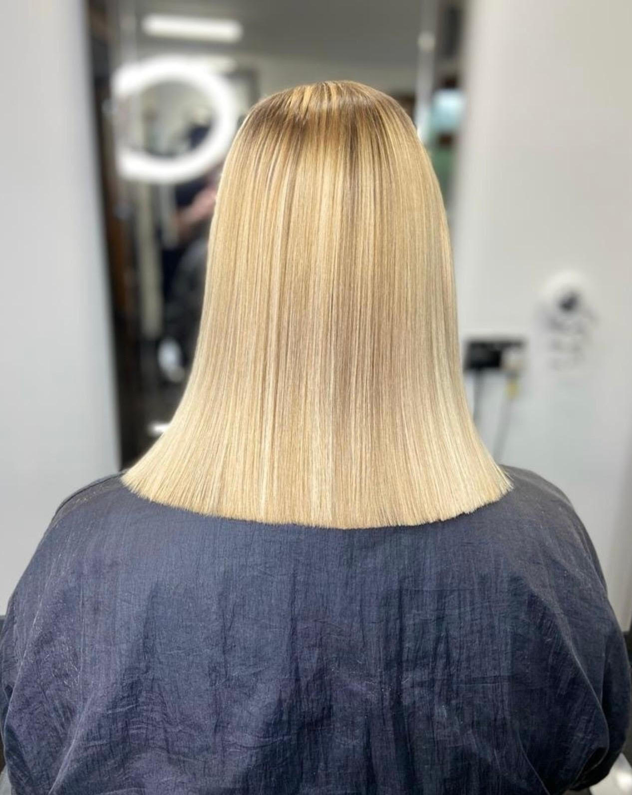 Back view of shoulder-length blonde hair with a blunt cut in a salon chair