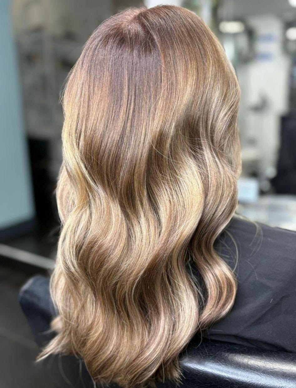 Long wavy blonde-brown hair styled in loose waves from the back in a salon chair