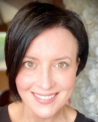 Close-up portrait of a smiling person with short dark hair against a soft blurred background