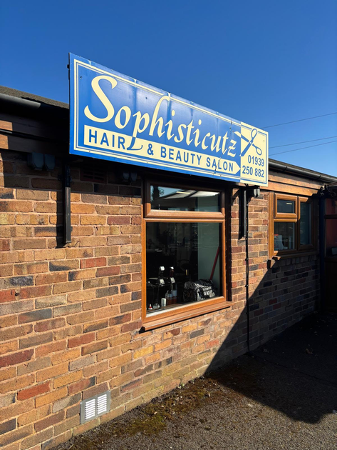 Blue “Sophistication Hair & Beauty Salon” sign on a brick building exterior